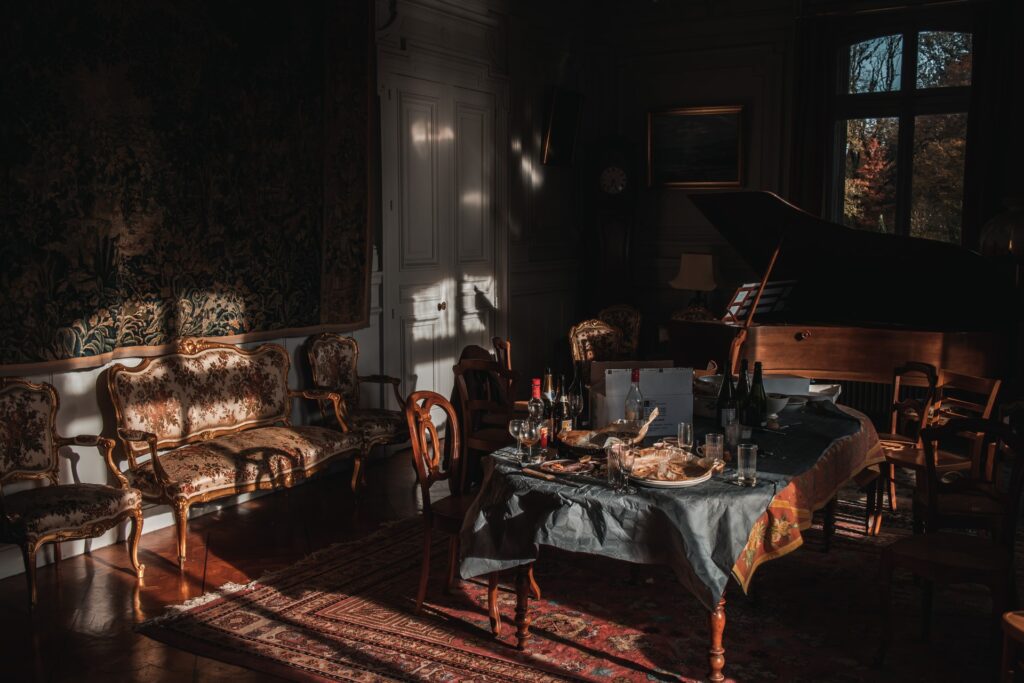 A dark room in a manor house with light shining onto the remains of a dinner party by the grand piano