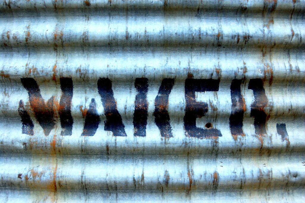 A piece of corrugated iron with the word "MAKER" stenciled on it to accompany a blog article by Delia Lloyd about figuring out if you're a Manager or a Maker.