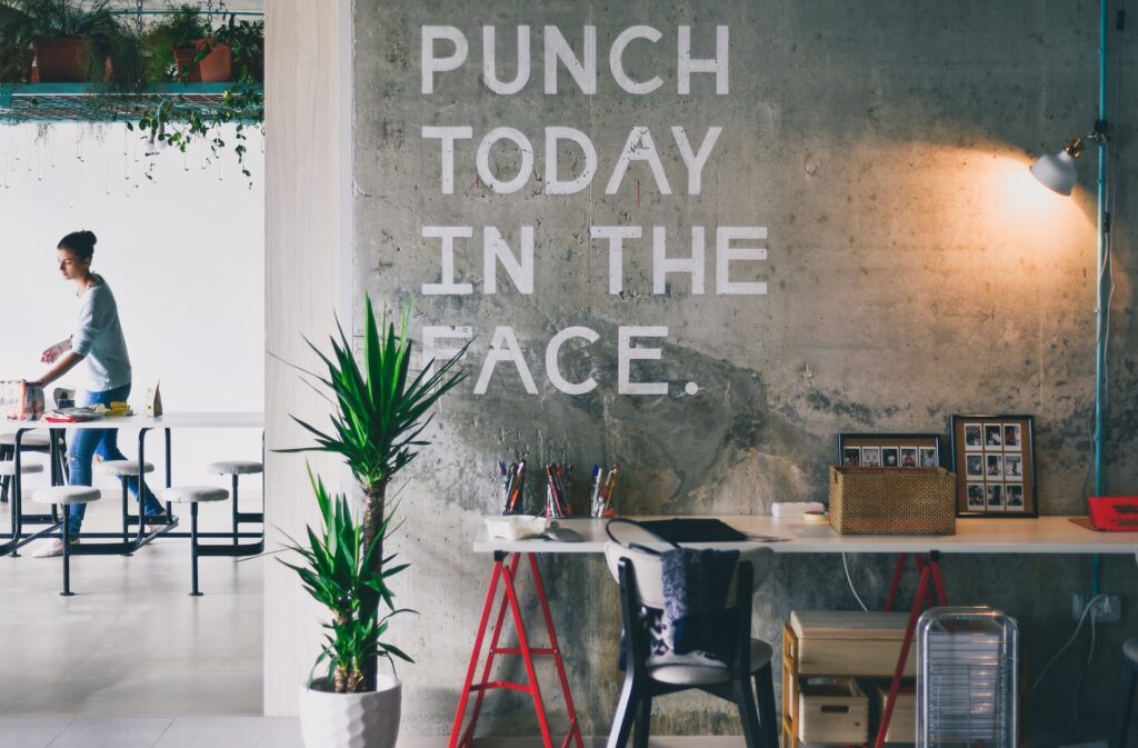 Designing your creative space. Image of a desk with the slogan "Punch Today in the face" written on the wall above it.
