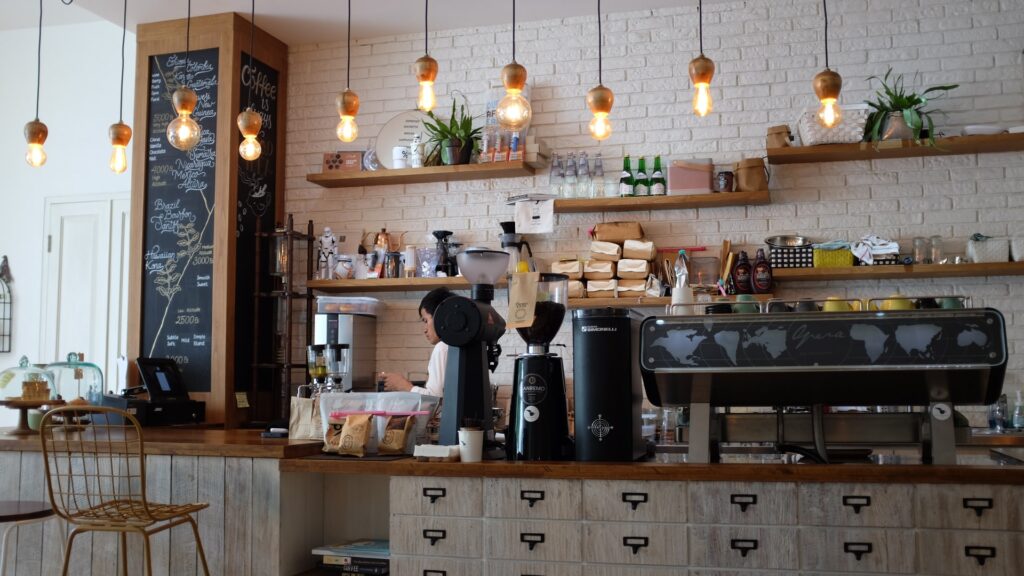 The counter in a neighbourhood coffee shop with modern lighting and a barista.