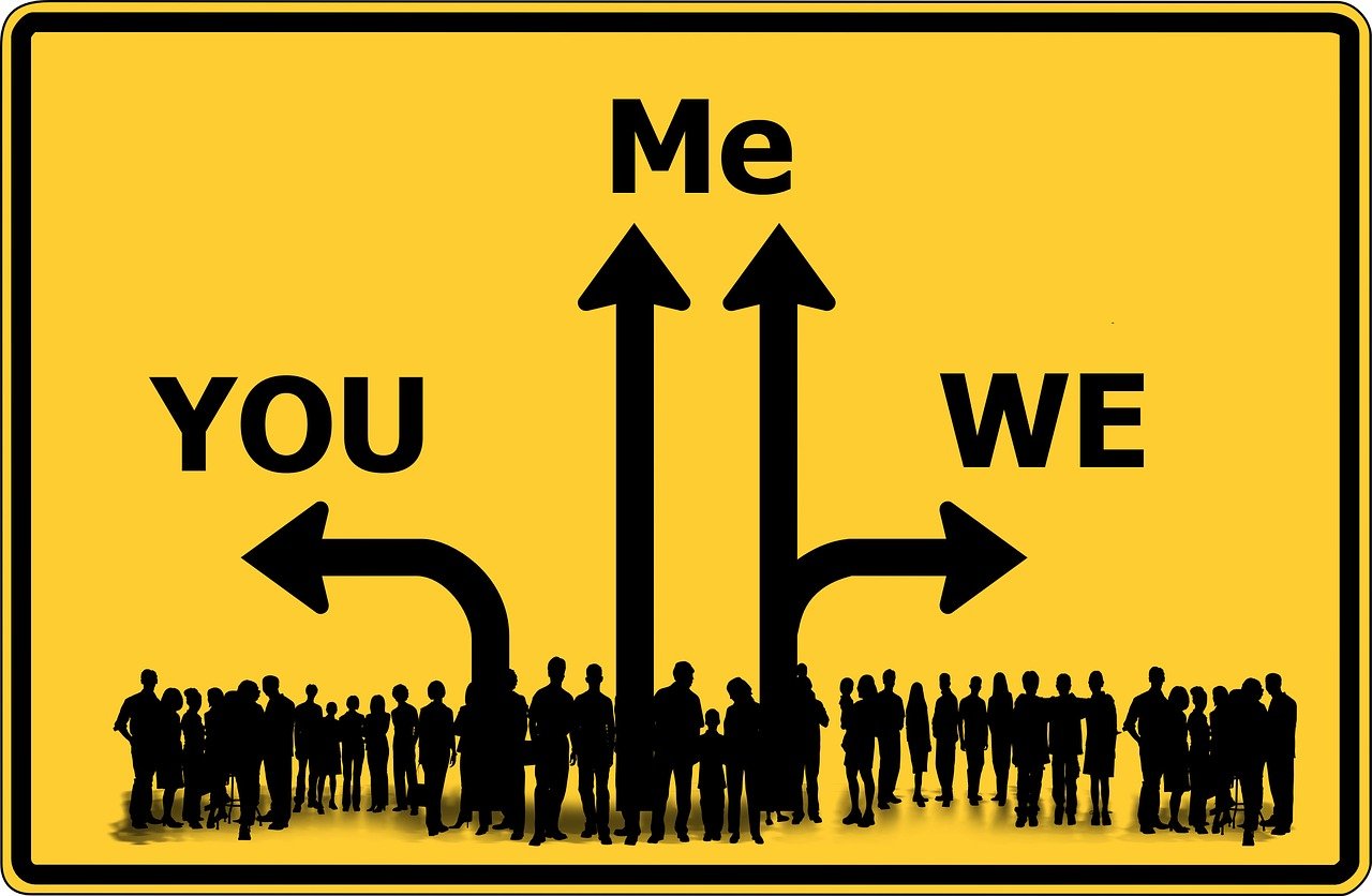 A yellow sign with a group of silhouetted people at the bottom with arrows saying You Me We.