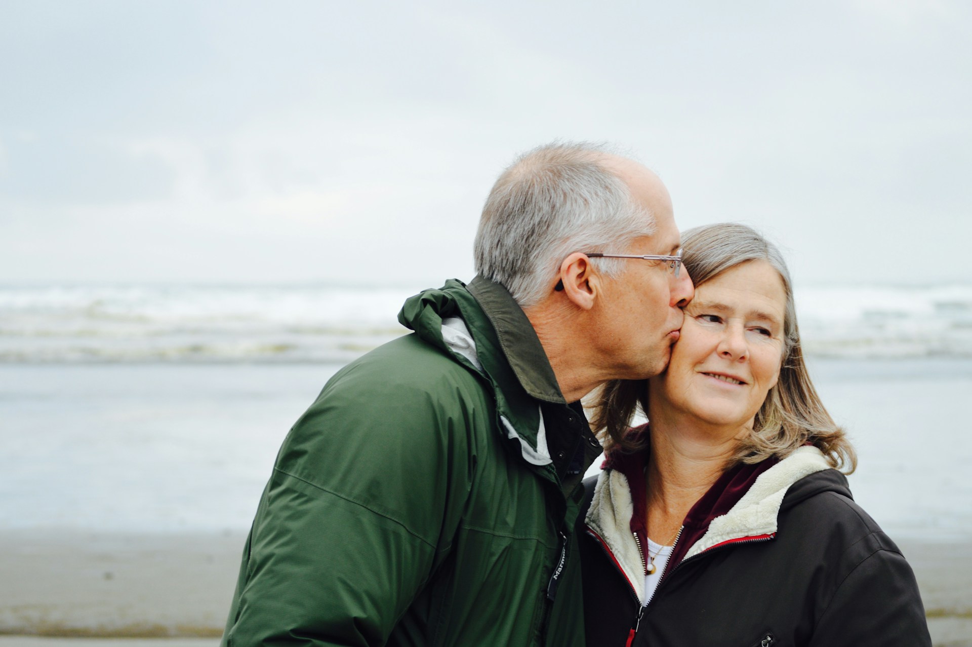 Older people and intimacy. Photo of a grey haried man kissing his partner on a beach.